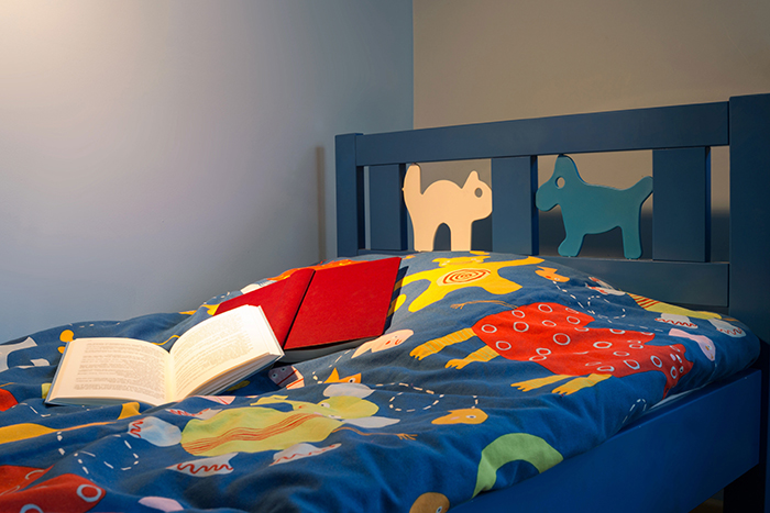 Cabecero de cama infantil en dormitorio con iluminación nocturna y dos libros encima de la cama