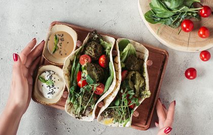 Manos de mujer sosteniendo un plato vegano hecho de tortillas, falafel, tomates cherry y semillas de girasol
