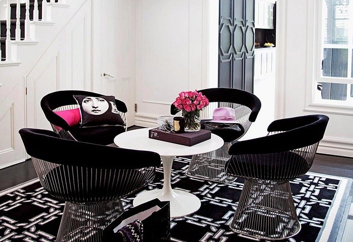Rincón de un hogar con mesa blanca con cuatro sillas negras y cojín