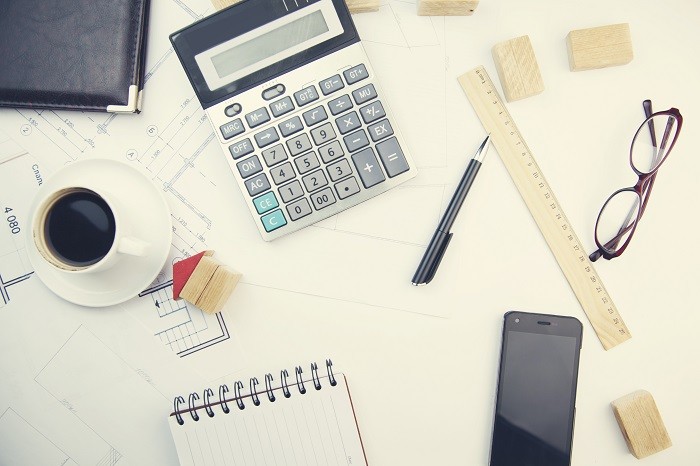 mesa de trabajo con calculadora para tasación de vivienda, café, gafas, móvil, bolígrafo y libreta