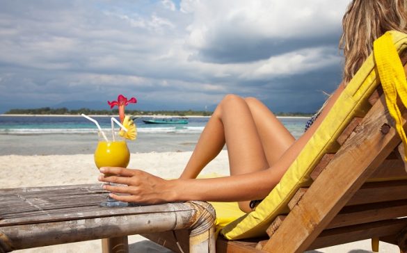 mujer en la playa sentada en una tumbona y tomando un cocktail