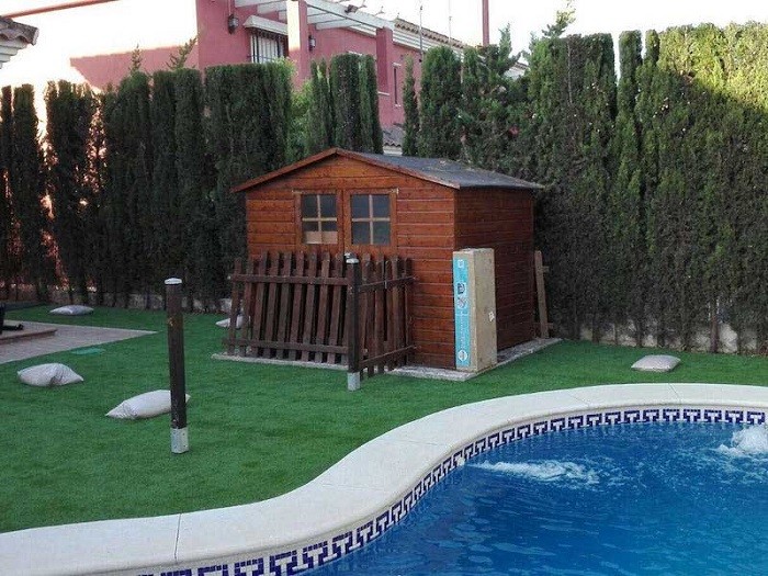 piscina con césped artificial y caseta de madera