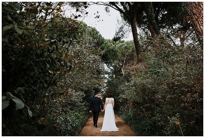 Fotografía de recién casados de espalda en un camino con árboles
