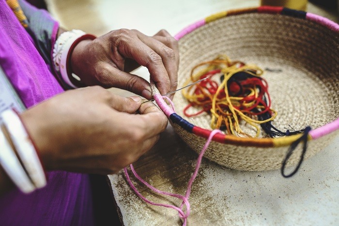 Manos de mujer cosiendo una cesta de fibras naturales con bordes de colores