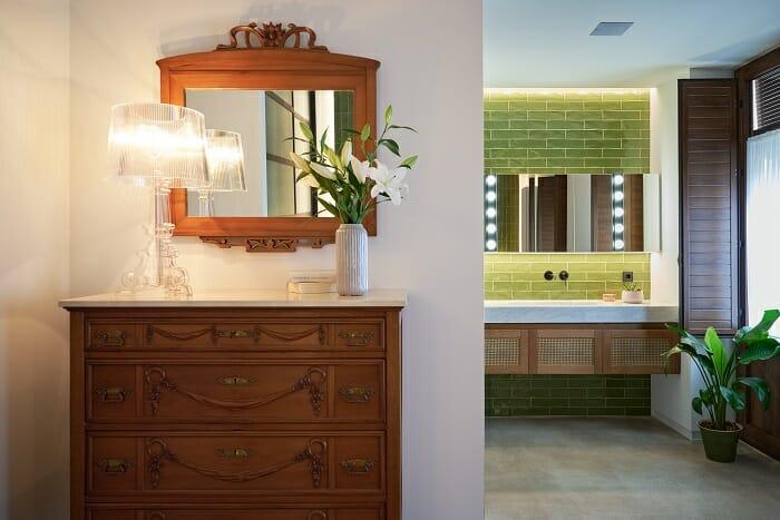 entrada con mueble de madera y espejo y de fondo lavabo con azulejos verde oliva de un piso reformado