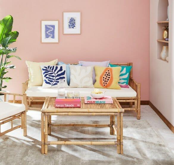 Salón con sofá con cojines de diferentes estilos, mesa de bambú y pared rosa palo