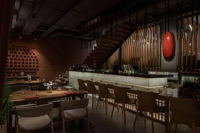 barra con mesas y taburetes del restaurante Tanuki con un huevo rojo en la pared como decoración japonesa