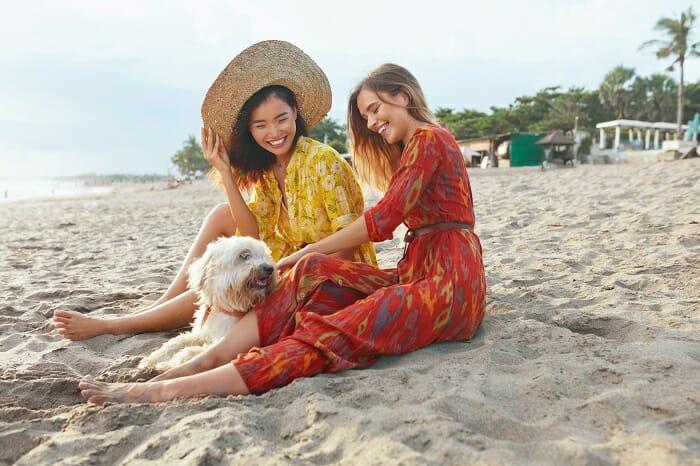 Dos chicas con vestidos sentadas en la playa con un perro