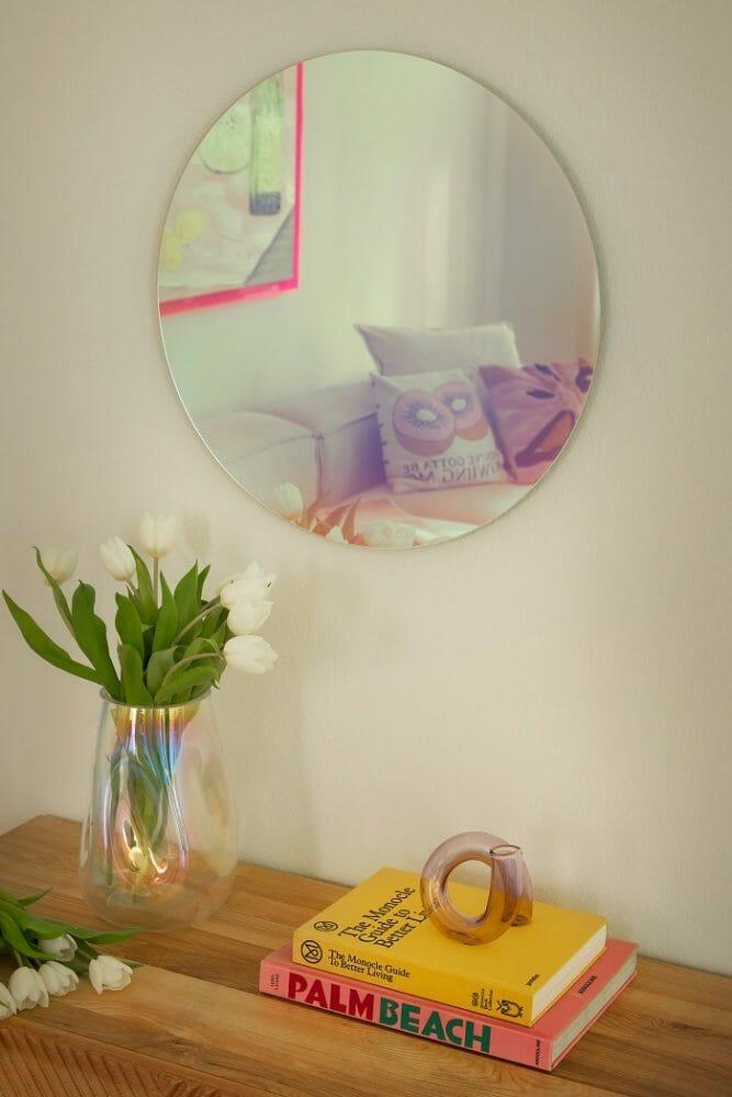 Jarrón, libros y un elemento decorativo encima de una mesa y en la pared un espejo redondo