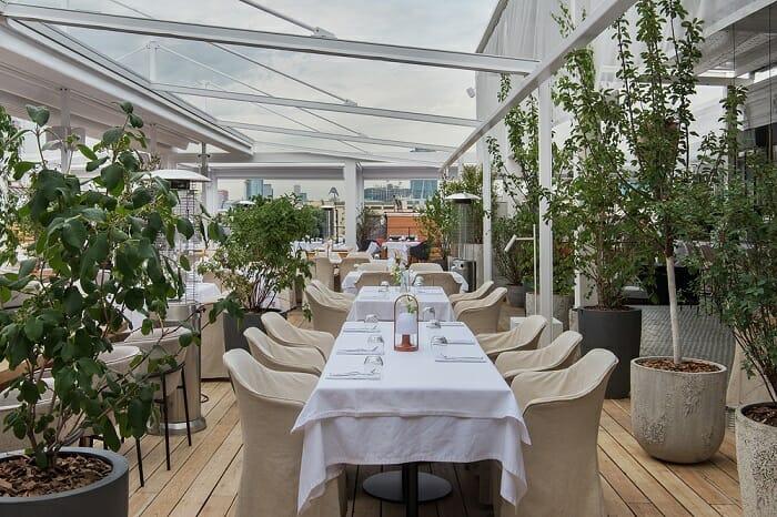 grandes mesas con sillas en la terraza del restaurante Peach con vegetación
