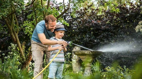 Padre e hijo regando el jardín de su casa con manguera Bosch