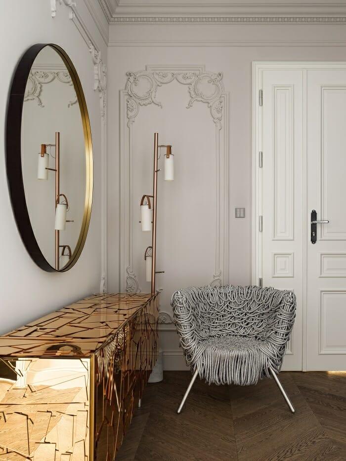 Entrada a un piso clásico con una cómoda dorada de diseño, un espejo redondo y una silla moderna