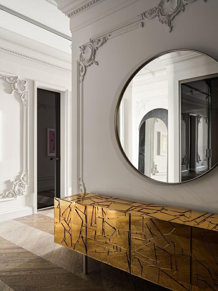 Entrada a un piso de diseño clásico con cómoda dorada y espejo redondo