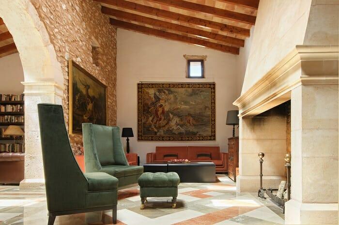 Sala de estar con vigas de madera en el techo, cuadros en las paredes, chimenea y sofás verdes