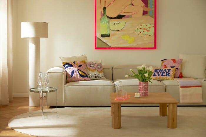 sofá en tono beige con cojines de colores y cuadro colorido estilo Barbiecore