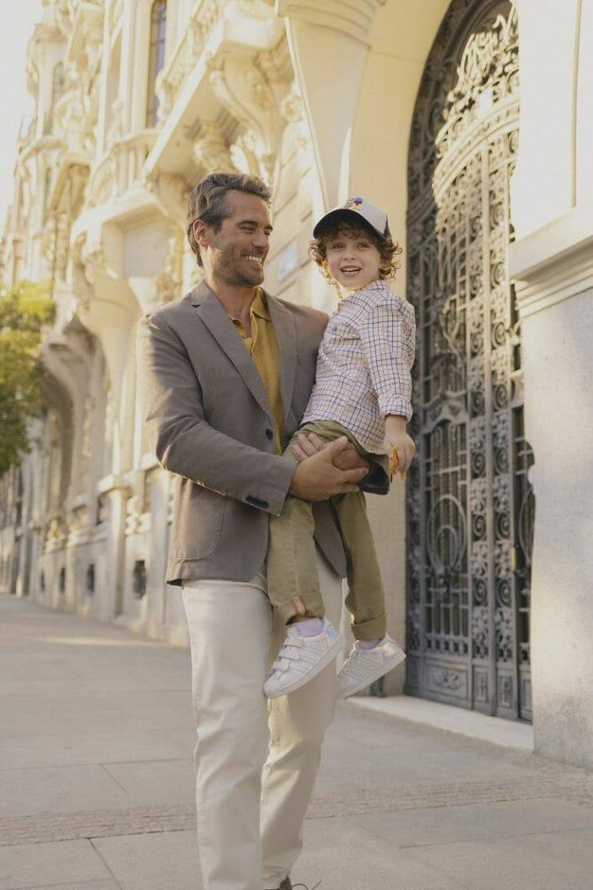 Padre llevando a su hijo en brazos por la calle y ambos llevan un estilo de ropa de la marca Scotta
