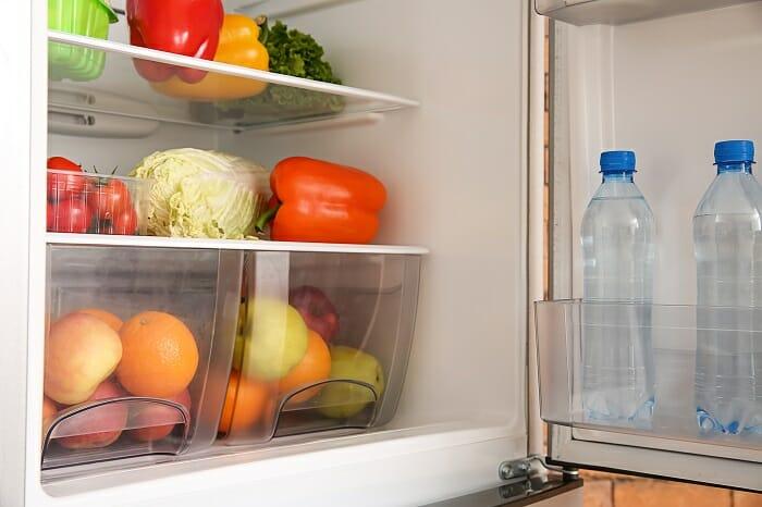 Interior de un frigorífico lleno de frutas, verduras y botellas de agua