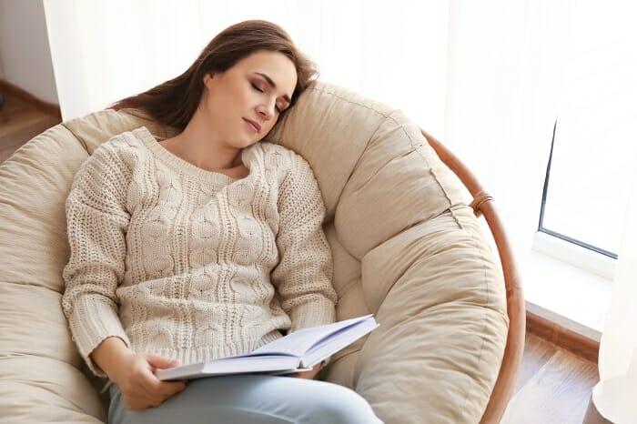 Chica que se ha quedado dormida leyendo un libro en un sillón cómodo