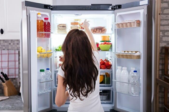 Chica frente a un frigorífico abierto lleno de alimentos