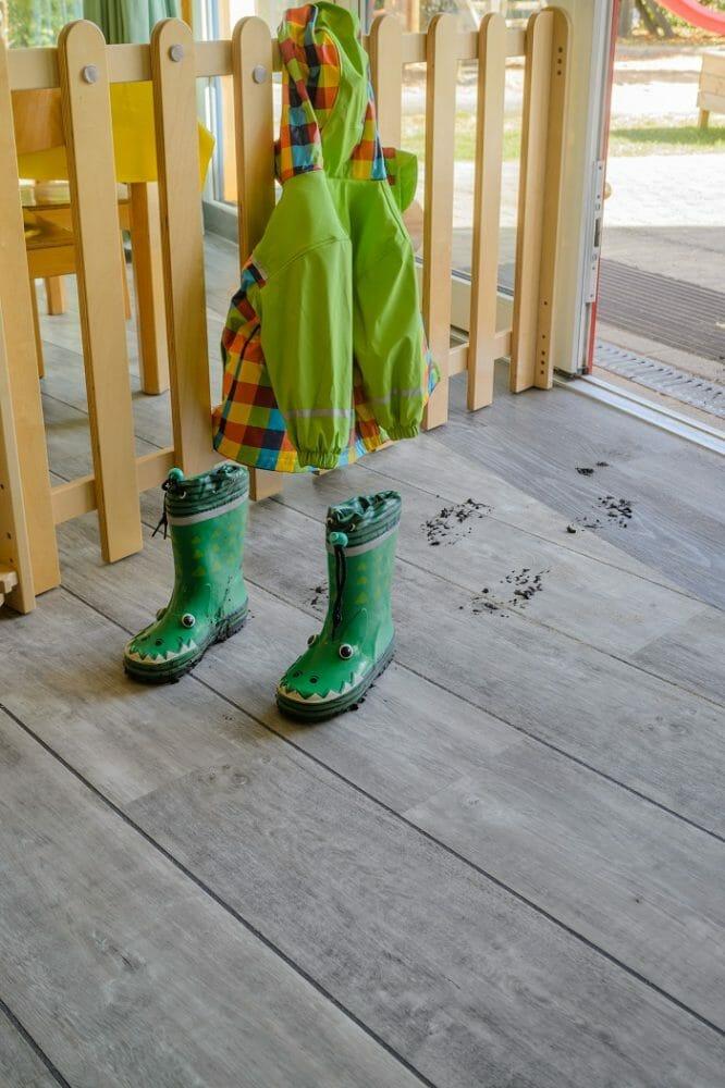 Chubasquero de un niño colgado y unas botas de agua infantiles sobre un pavimento gris