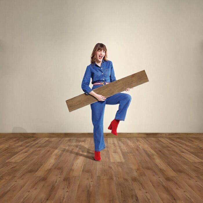 Mujer en una sala con un suelo de madera y ella sostiene una lámina de madera del suelo