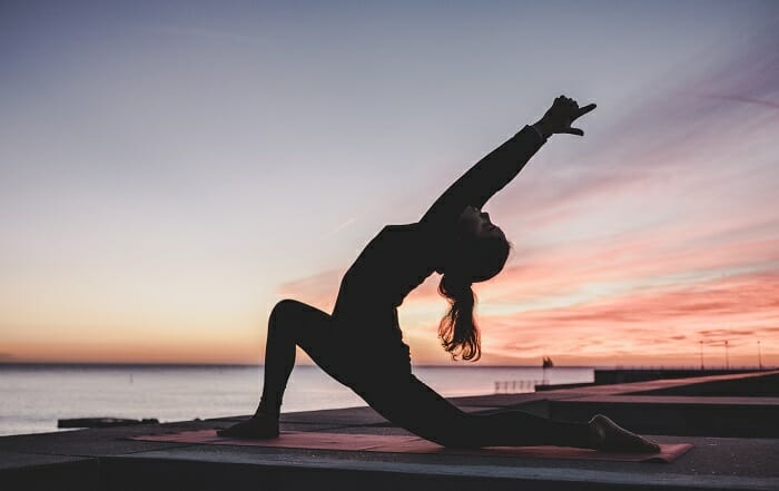Silueta de mujer haciendo yoga al lado del mar mientras anochece