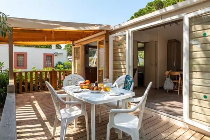 Terraza de una casa de camping con mesa y sillas de plástico y con un desayuno