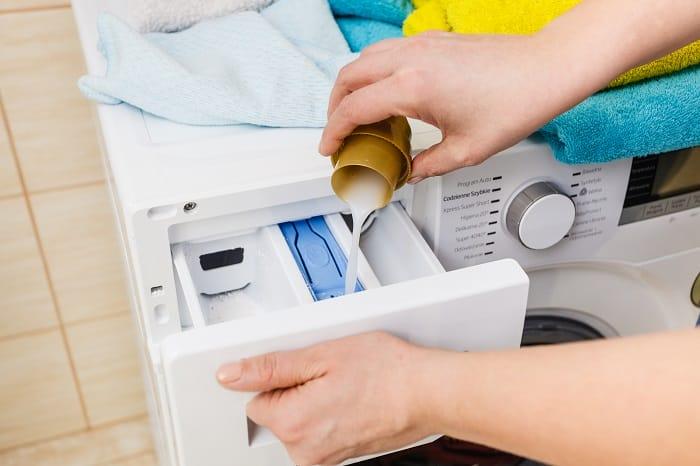 Mujer echando detergente líquido al cajetín de la lavadora
