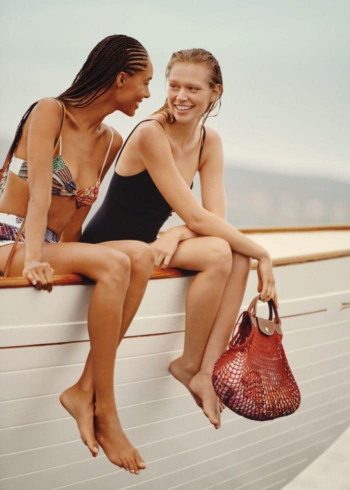Dos modelos sentadas en un barco con bañadores y un bolso Longchamp