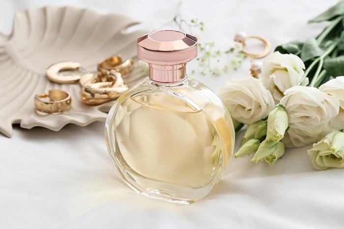 Bote de perfume encima de la mesa con ramo de rosas blancas
