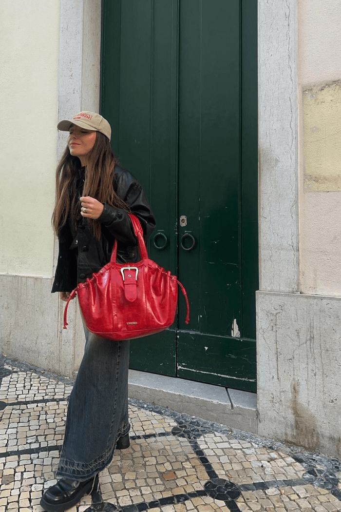Modelo en la calle con gorra y un bolso rojo grande
