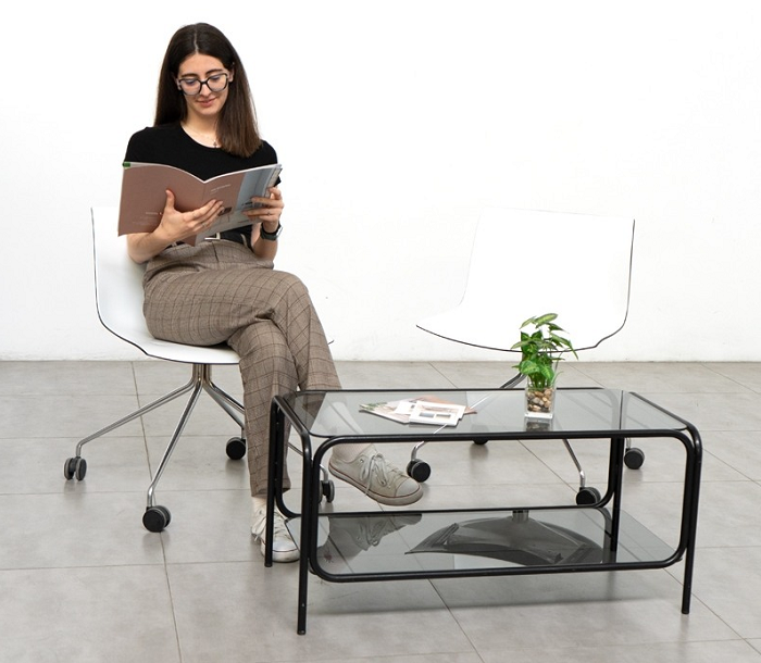 Sala de espera con una mujer sentada leyendo una revista y una mesa de cristal con estructura en negro