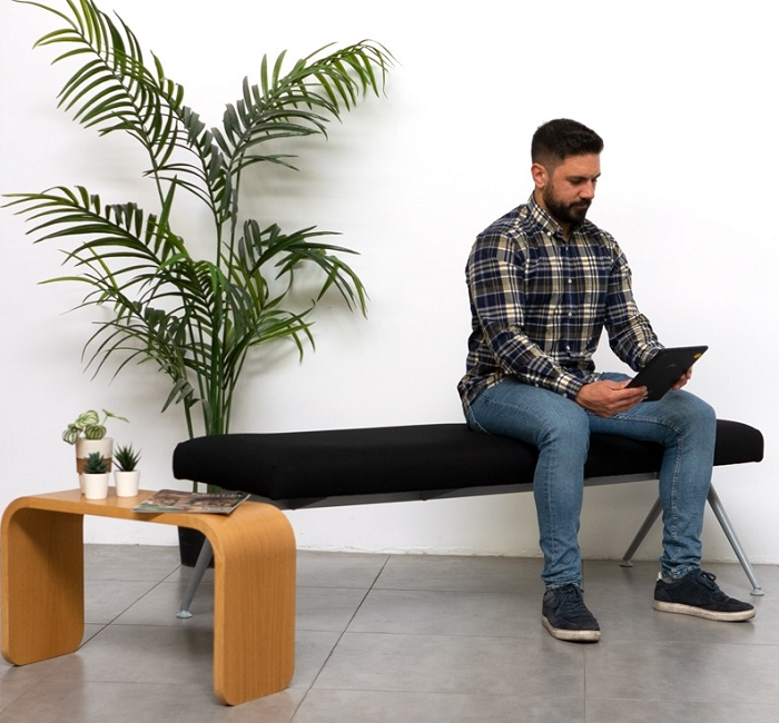 Hombre leyendo y sentado en una sala de espera con una mesa baja auxiliar de madera curva